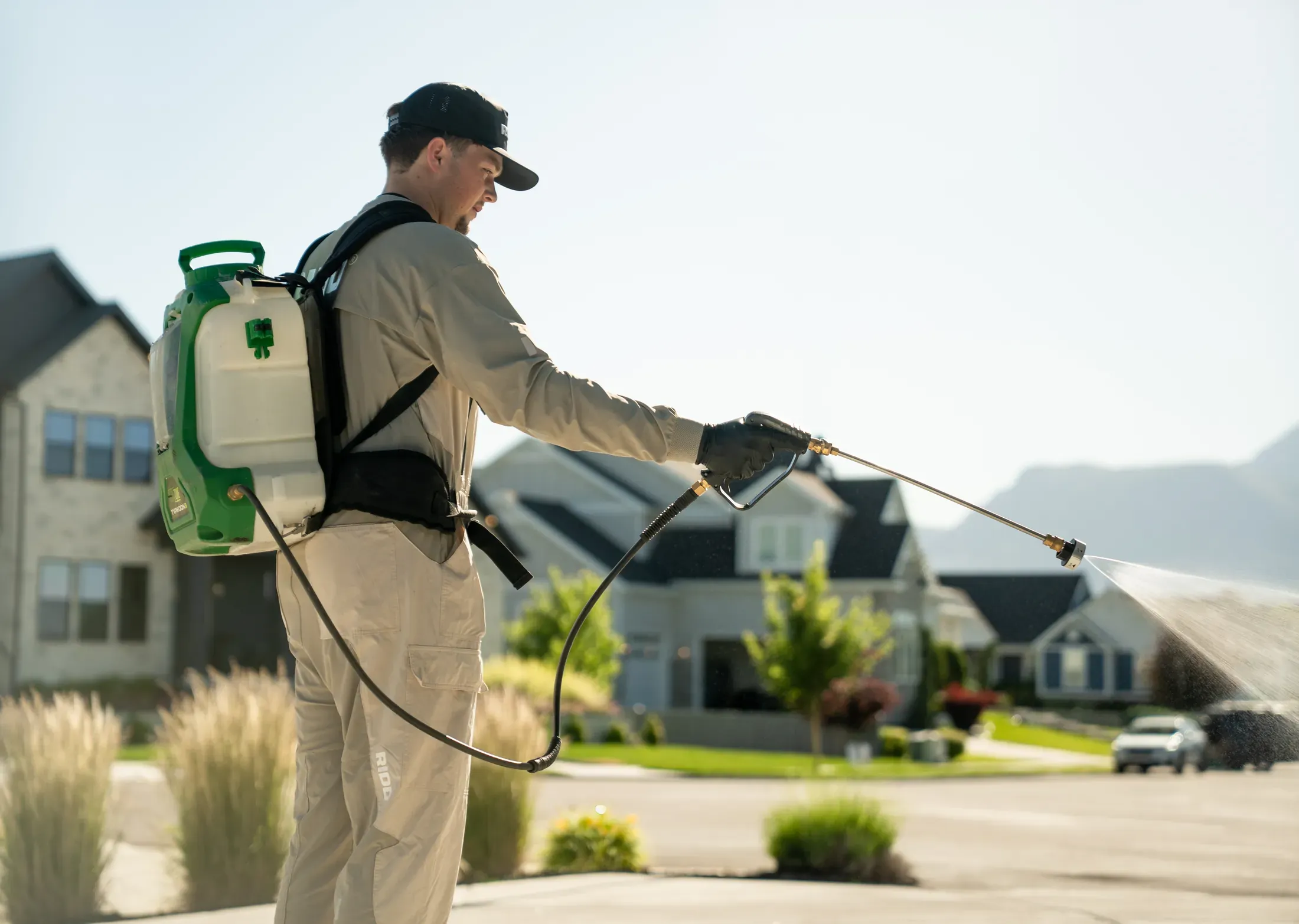 A RIDD technician applying an exterior pest control treatment near a residential yard.